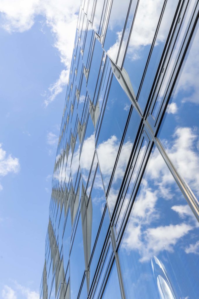 Gläserne Hausfassade spiegelt Himmel mit Wolken